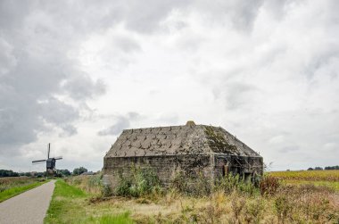 Sleeuwijk, Hollanda, 2 Ekim 2021: Arka planda yel değirmeni olan beton sığınak, her ikisi de tarihi Hollanda Waterline dünya mirasının bir parçası.