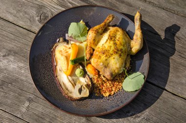 Bir tabak dolusu kızarmış tavuk ve çeşitli sebzelerle güneşli bir terasta ahşap bir masada.