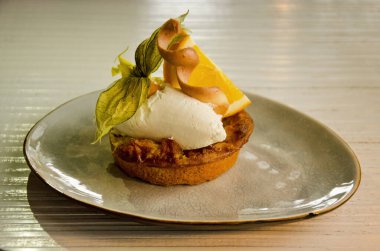 Küçük yuvarlak bir elmalı turta, krema ve ahşap bir restoran masasında bir parça portakal.