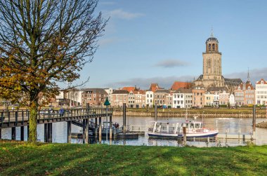 Deventer, Hollanda, 13 Kasım 2021: bir ağaç, bir iskele ve bir feribot ve ötesinde IJssle nehri ve kasabanın manzaralı kıyı şeridi.