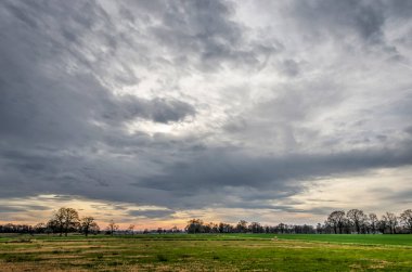 Dramatic sky over a flat landscape with fields, meadows and scattered trees and bushes near Hardenberg, The Netherlands