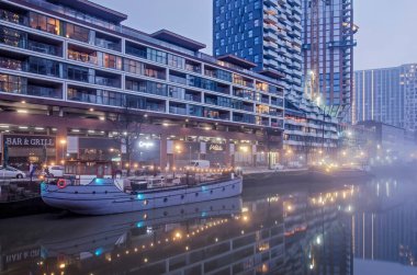 Rotterdam, Hollanda, 12 Ocak 2022: kısmen yapım aşamasında olan modern konut binaları ve tarihi gemiler sisli bir sabahta Wijnhaven limanının durgun sularına yansıyor.