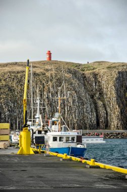 Stykkisholmur, İzlanda, 3 Mayıs 2022: Limanın rıhtımı boyunca demirli tekneyle ve arka planda deniz feneriyle birlikte kayanın görüntüsü