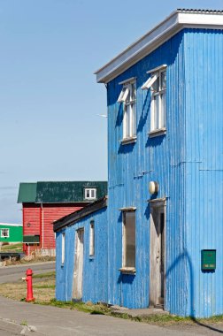 Hvammstangi, İzlanda, 1 Mayıs 2022: Arka planda kırmızı ve yeşil bir ev bulunan mavi kıvrımlı metal cepheli karakteristik ev