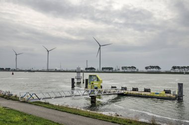 Rotterdam, Hollanda, 23 Eylül 2022: Nieuwe Waterweg kanalında yüzen çelik iskele, arka planda üç rüzgar türbini.