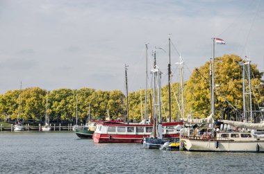 Enkhuizen, Hollanda, 4 Ekim 2022: Buitenhaven 'da (Dış Liman) arka planda sonbahar renklerinde kül ağaçları olan tekneler