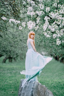 Bahçede çırpınan elbiseli kızıl saçlı genç kız. 