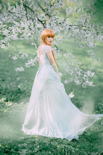 Young redhead girl in fluttering dress in the garden