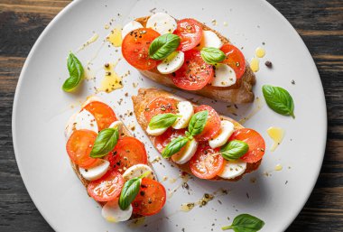 bruschetta caprese. Taze fesleğen yaprakları, olgun aromatik domatesler ve bruschetta üzerine İtalyan mozzarella, zeytin yağı serpiştirilmiş ve biber ve bitkilerle serpilmiş..