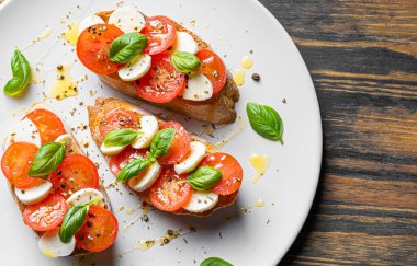 bruschetta caprese. Taze fesleğen yaprakları, olgun aromatik domatesler ve bruschetta üzerine İtalyan mozzarella, zeytin yağı serpiştirilmiş ve biber ve bitkilerle serpilmiş..