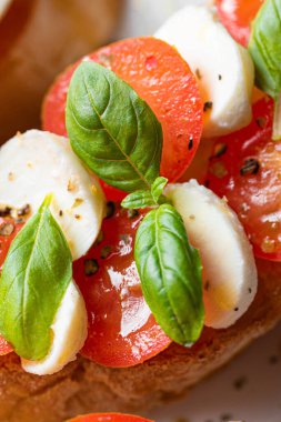 bruschetta caprese. Taze fesleğen yaprakları, olgun aromatik domatesler ve bruschetta üzerine İtalyan mozzarella, zeytin yağı serpiştirilmiş ve biber ve bitkilerle serpilmiş..
