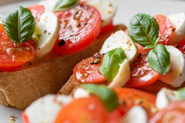 bruschetta caprese. Taze fesleğen yaprakları, olgun aromatik domatesler ve bruschetta üzerine İtalyan mozzarella, zeytin yağı serpiştirilmiş ve biber ve bitkilerle serpilmiş..