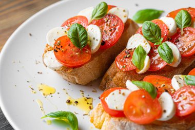 bruschetta caprese. Taze fesleğen yaprakları, olgun aromatik domatesler ve bruschetta üzerine İtalyan mozzarella, zeytin yağı serpiştirilmiş ve biber ve bitkilerle serpilmiş..