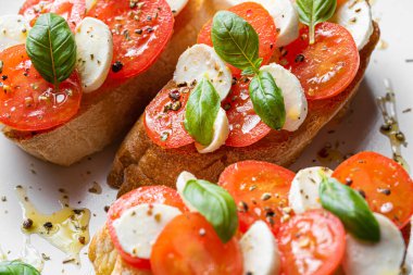 bruschetta caprese. Taze fesleğen yaprakları, olgun aromatik domatesler ve bruschetta üzerine İtalyan mozzarella, zeytin yağı serpiştirilmiş ve biber ve bitkilerle serpilmiş..