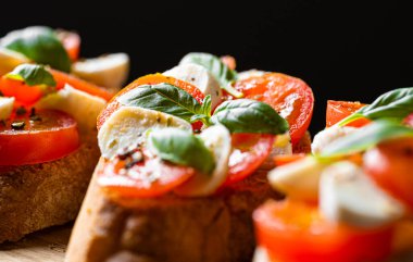 bruschetta caprese. Taze fesleğen yaprakları, olgun aromatik domatesler ve bruschetta üzerine İtalyan mozzarella, zeytin yağı serpiştirilmiş ve biber ve bitkilerle serpilmiş..