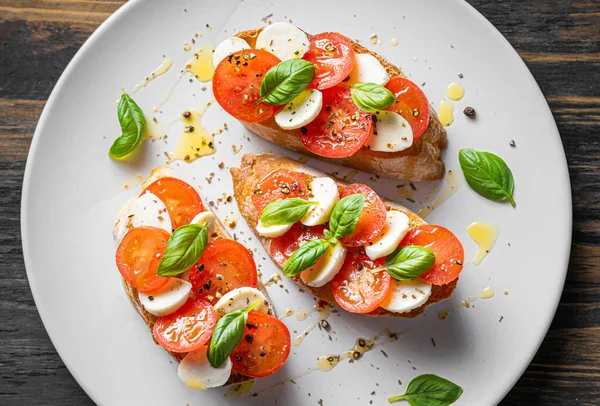 bruschetta caprese. Taze fesleğen yaprakları, olgun aromatik domatesler ve bruschetta üzerine İtalyan mozzarella, zeytin yağı serpiştirilmiş ve biber ve bitkilerle serpilmiş..