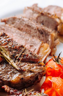 Sulu, iyi pişmiş pirzola biftekleri, siyah ahşap bir tabakta, üstünde gramer ve kızarmış kiraz domatesleri ve biberli.