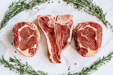 Beyaz mermer yüzeyde ızgara yapmaya hazır üç lezzetli biftek.