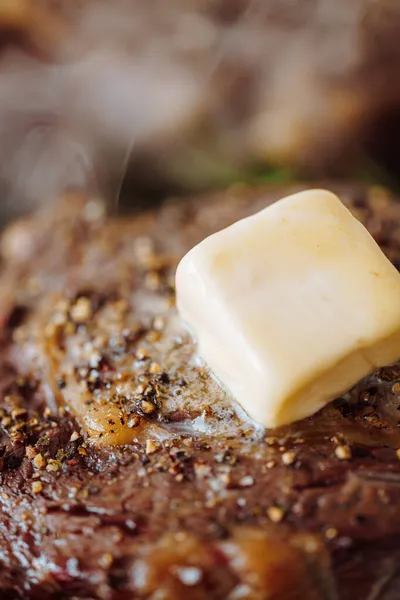 グランドペッパーとローズマリーの小枝と塩で味付けステーキにバターが広がってグリルパンで豪華なステーキを調理します — ストック写真