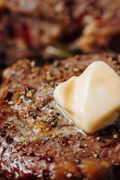 グランドペッパーとローズマリーの小枝と塩で味付けステーキにバターが広がってグリルパンで豪華なステーキを調理します — ストック写真