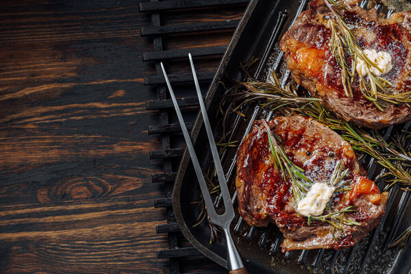 cooking sumptuous steaks in a grill pan with butter spreading over the steak seasoned with ground pepper and salt with rosemary sprigs