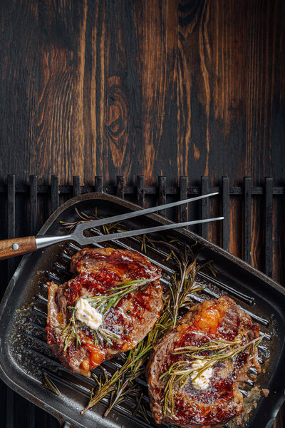 cooking sumptuous steaks in a grill pan with butter spreading over the steak seasoned with ground pepper and salt with rosemary sprigs