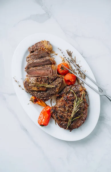 Beyaz mermer bir yüzey üzerinde beyaz bir tepside kızarmış pirzola biftekleri ve ahududu, vişneli domates ve biber. Biftekler dilimlendi ve servis için hazır.