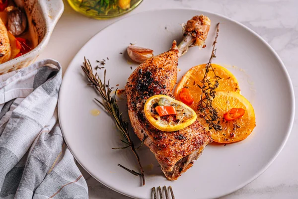 roasted fried turkey duck thighs, rubbed with spices and salt, on a baking sheet, with oranges, lemons, garlic, rosemary, thyme and olive oil. the concept of a healthy and tasty dinner for two.