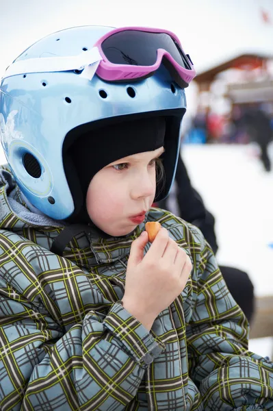 Little girl in ski helmet eats sausage — Stock Photo, Image