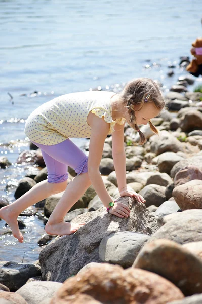 Meisje klimmen op stenen door kust — Stockfoto