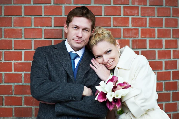 Glückliche Braut und Bräutigam vor roter Backsteinmauer — Stockfoto