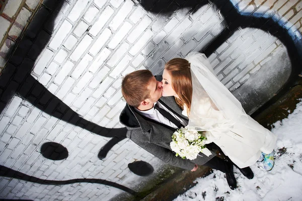 Beijar noiva e noivo perto da parede de tijolo com graffiti — Fotografia de Stock