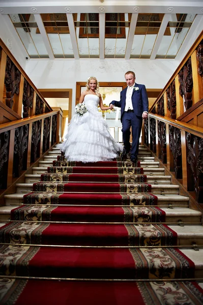 Élégant marié et mariée dans des escaliers de luxe avec tapis rouge — Photo