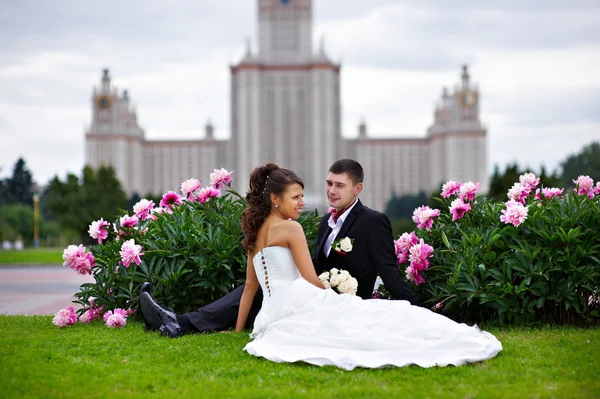 Novia romántica y novio en el parque rodeado de flores de peonía — Foto de Stock