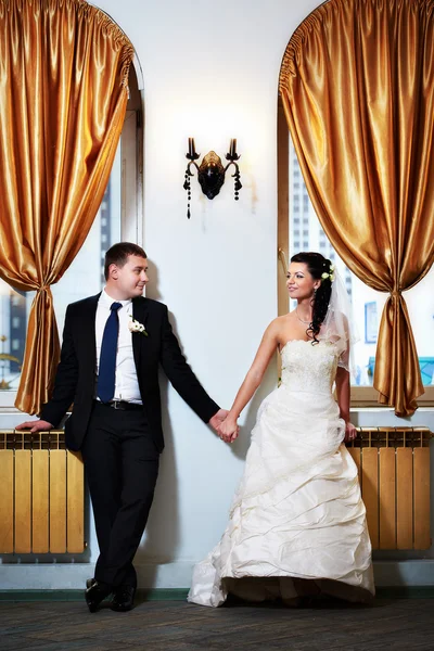 Happy bride and groom hold each other's hand near beautiful wind — Stock Photo, Image