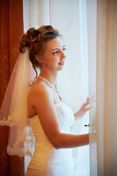 Hermosa novia en vestido de novia cerca de la ventana — Foto de Stock