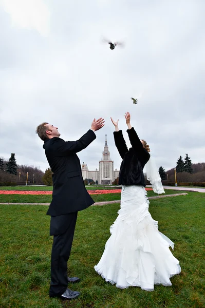 Happy bride and groom issue from the hands of pigeons — Stock Photo, Image