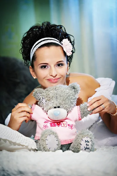 Gelukkige bruid met teddy bear op witte bed — Stockfoto