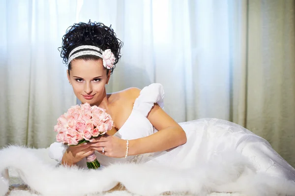 Beautiful bride with bouquet of flowers on white bed — Stock Photo, Image