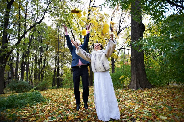 Joyful bride and groom throw the yellow leaves — Stock Photo, Image