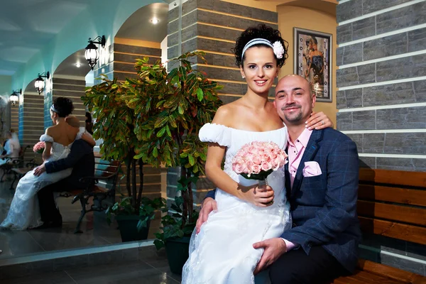 Glückliche Braut und Bräutigam auf Holzbank im modernen Interieur — Stockfoto