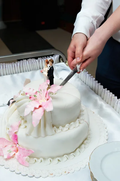 Brudgummen och bruden skär bröllopstårta med rosa blommor — Stockfoto