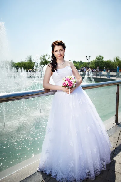 Happy bride about fountain with bouquet — Stock Photo, Image