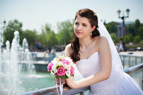 Happy bride about fountain with bouquet — Stock Photo, Image