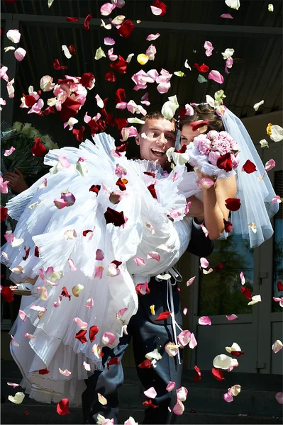 Happy newlyweds and flying red and white petals — Stock Photo, Image