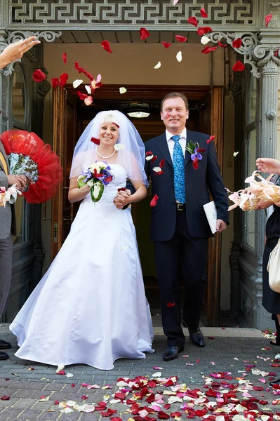 Happy newlyweds and flying red petals — Stock Photo, Image