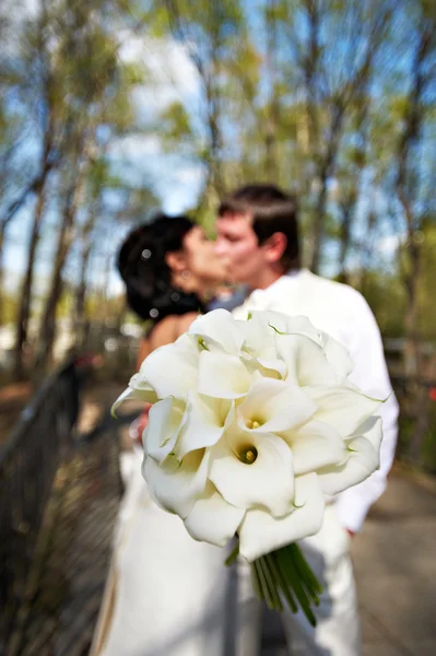 Bouquet kala against romantic kiss bride and groom — Stock Photo, Image