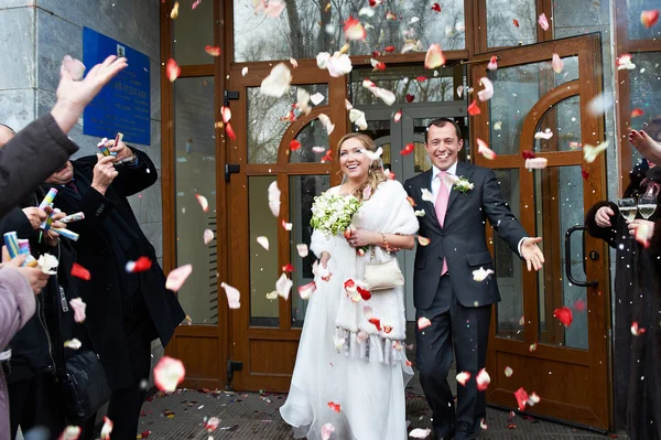 Sposi felici con ospiti e petali volanti — Foto Stock