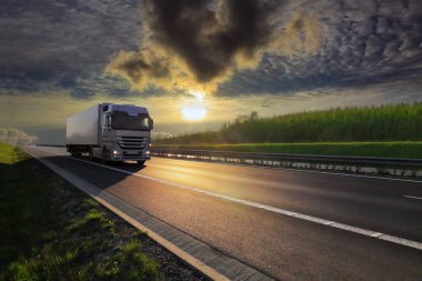 Landscape with a moving truck on the highway at sunset.