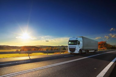 Landscape with a moving truck on the highway at sunset.